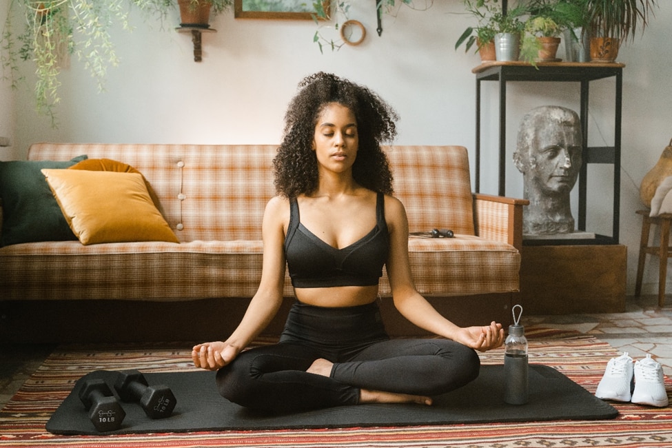 Oturma odasında yoga yaparken huzurlu ve sağlıklı görünen bir kadın.